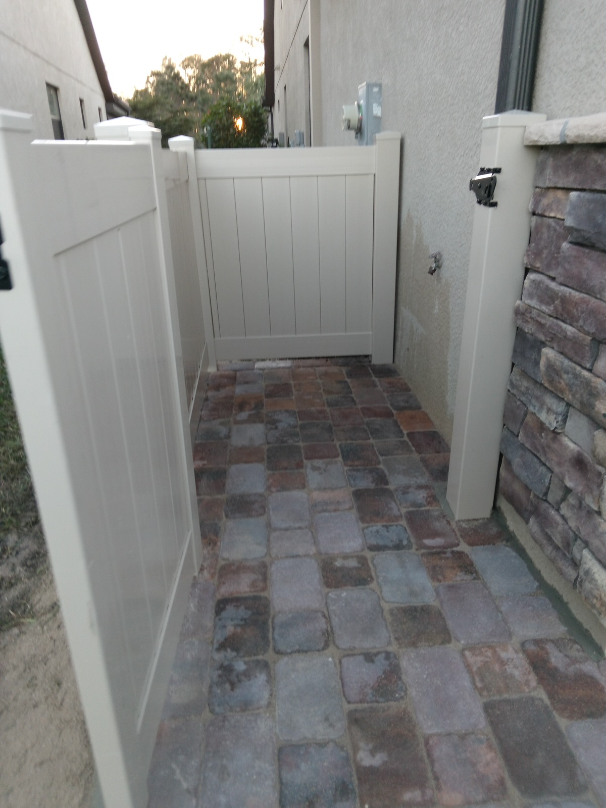 Cobblestone paver side yard with white vinyl privacy gate